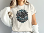 White t-shirt with kraken design, waves, mountains, and text "KRAKEN BEYOND THE DEPTHS".