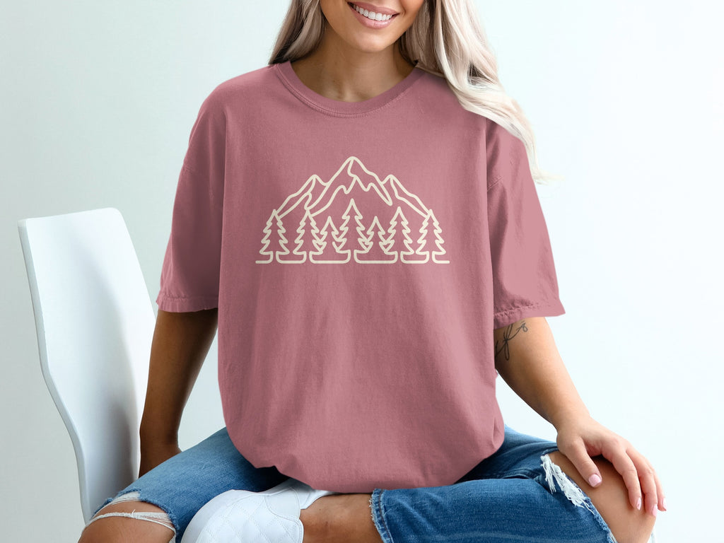 Pink t-shirt with a minimalist outline of mountains and pine trees on the front.
