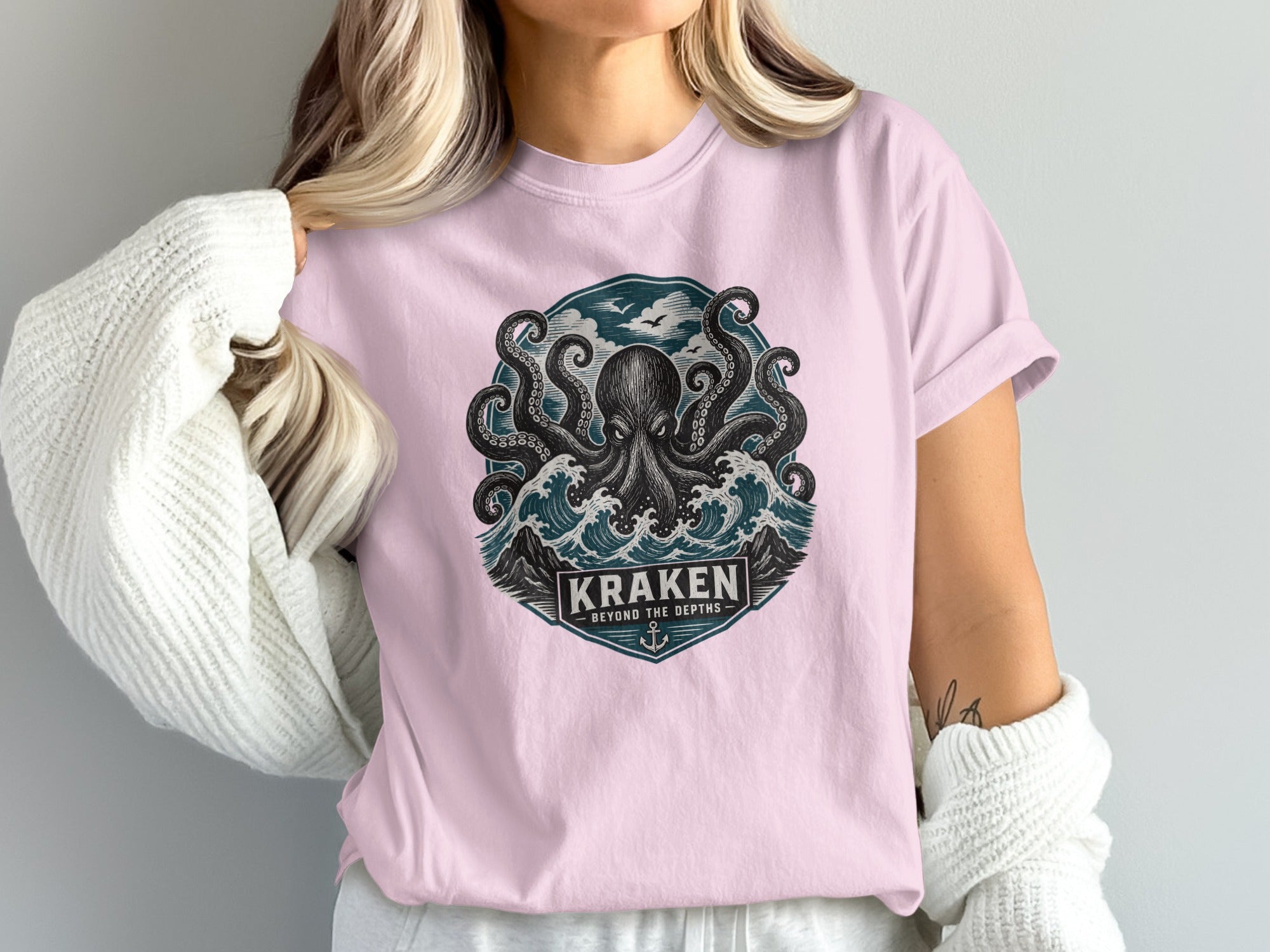 Pink t-shirt with Kraken octopus, waves, and text "KRAKEN BEYOND THE DEPTHS" designs.