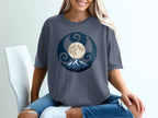 T-shirt with a moon, mountains, trees, and swirling blue design.