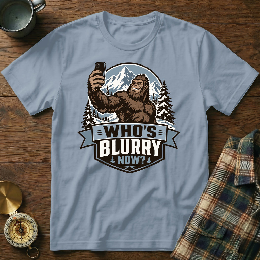 Bigfoot takes a selfie in the mountains with "Who's Blurry Now?" text.