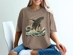 Brown t-shirt with graphic of a humpback whale breaching in ocean waves.