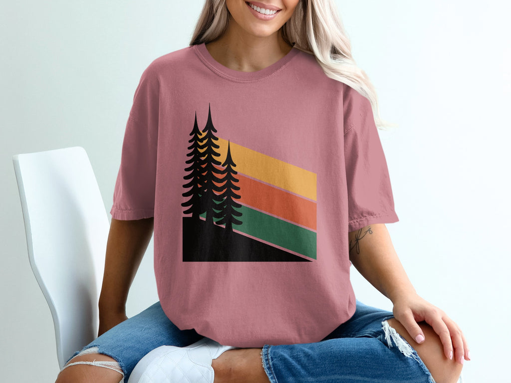 Woman wearing a pink t-shirt with a retro sunset and pine trees design.