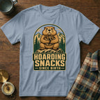 Groundhog hoarding snacks since birth, outdoor scene on a light blue t-shirt.