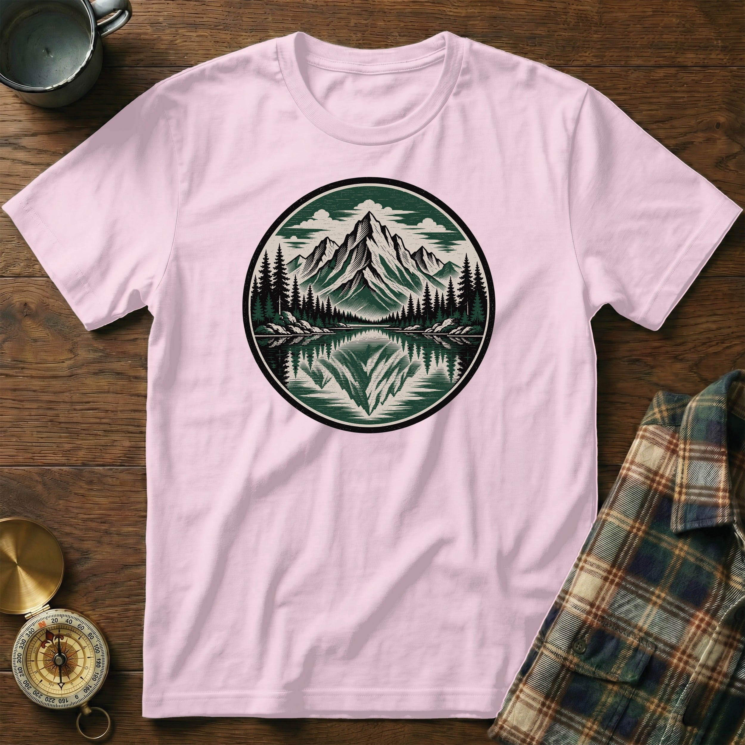 Pink t-shirt with a circular emblem of mountains, trees, and a lake reflection.