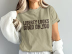 Tan t-shirt with brown text "LIBERTY LOOKS GOOD ON YOU" and graphic.