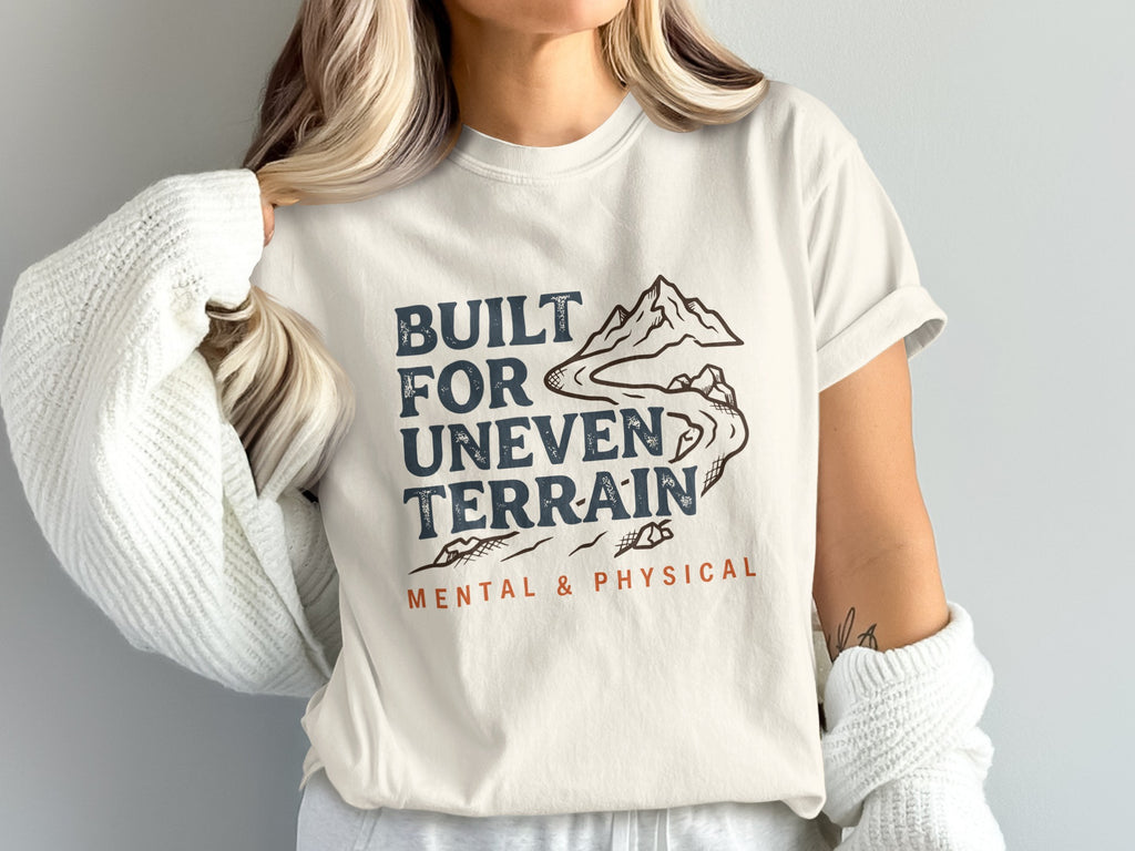 Cream t-shirt with "BUILT FOR UNEven TERRAIN MENTAL & PHYSICAL" and mountain graphic.