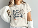 Cream t-shirt with "BUILT FOR UNEven TERRAIN MENTAL & PHYSICAL" and mountain graphic.