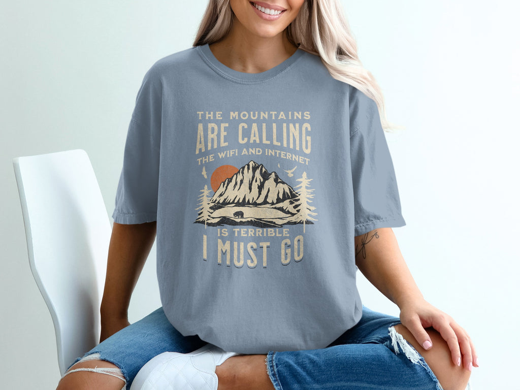 Graphic tee with mountains, sun, and text: "The mountains are calling..."