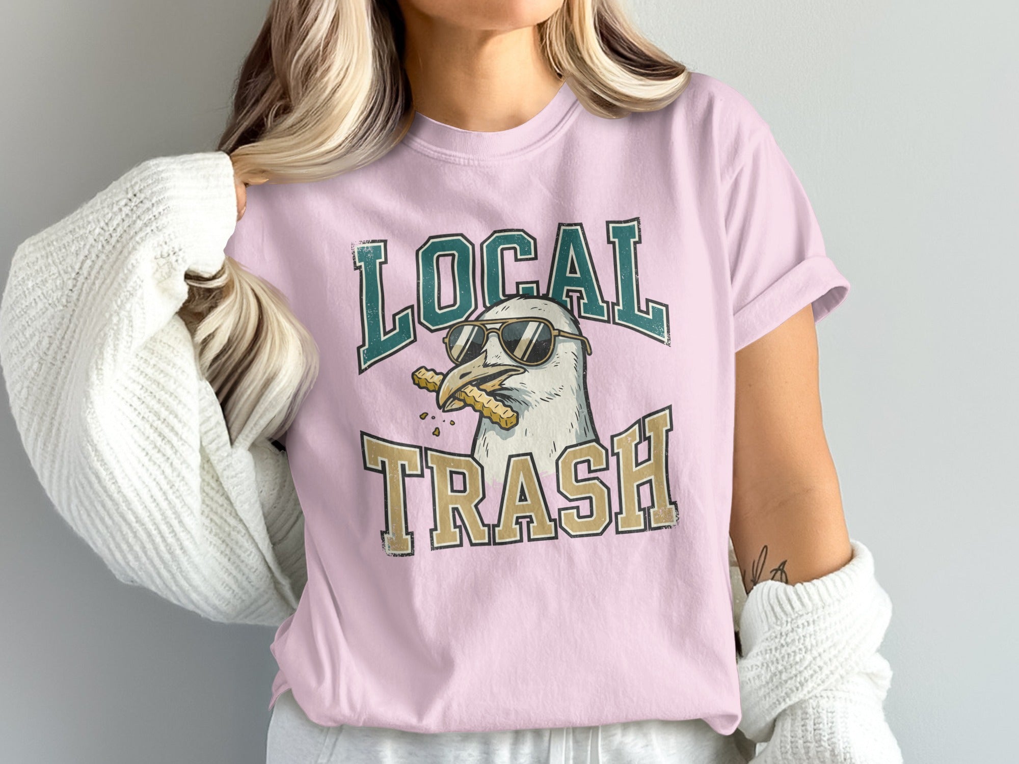 Pink t-shirt with a cartoon seagull wearing sunglasses and eating fries.