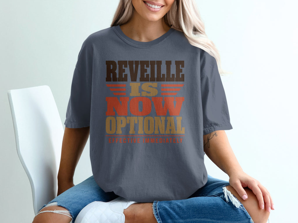 A blonde woman wearing a grey t-shirt with the brown and orange text "Reveille Is Now Optional".