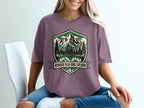 Purple t-shirt with a mountain, trees, and lake graphic that says "Nowhere Near Done Exploring".