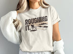 Cream t-shirt with "Roughing It" text and a beach scene illustration.