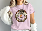 Pink t-shirt with "Survived Adult Conversation" merit badge graphic.