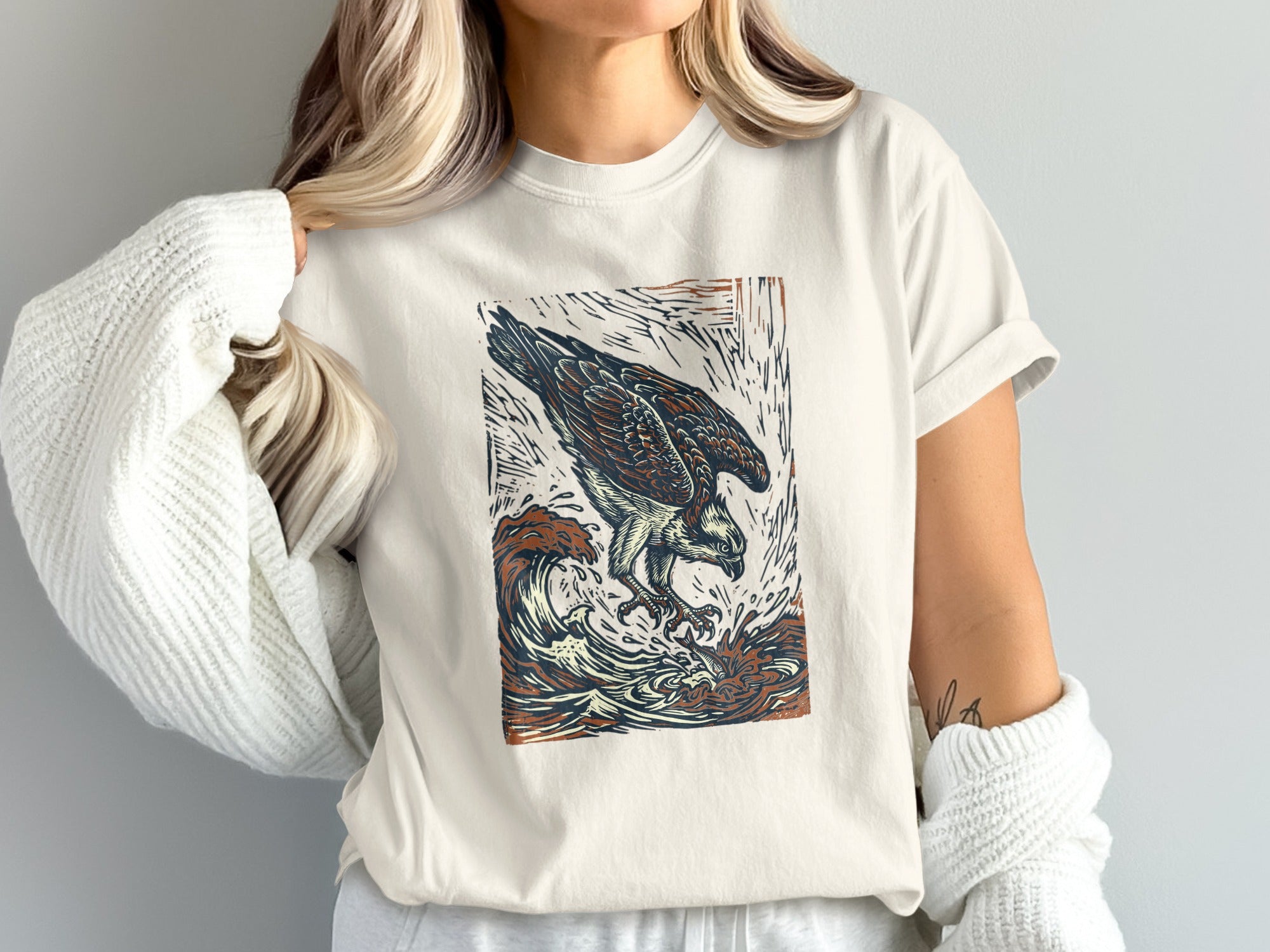White t-shirt with woodcut-style osprey diving into waves graphic.