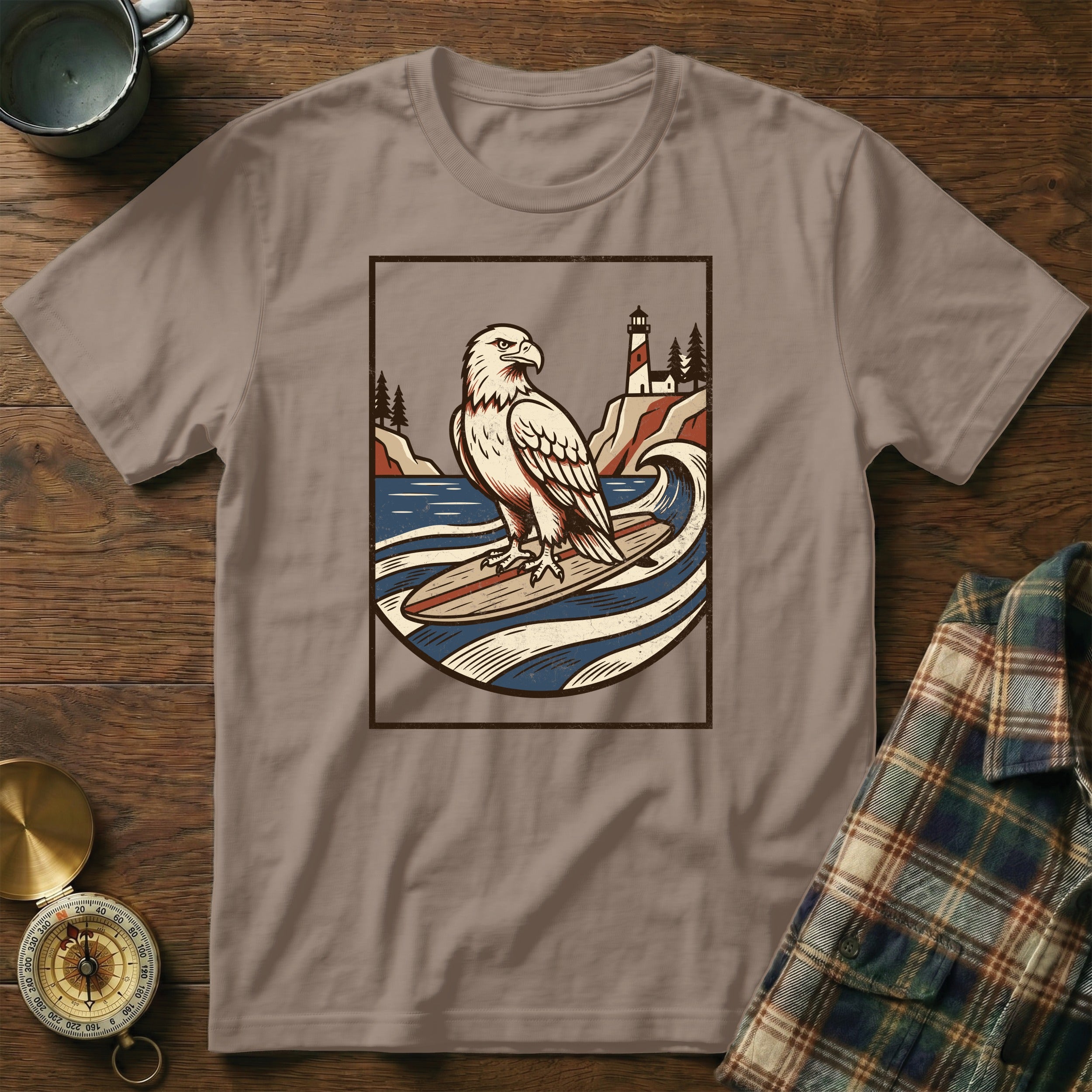 T-shirt with graphic of eagle on surfboard in front of lighthouse.
