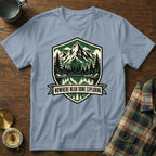 Light blue t-shirt with shield graphic of mountains, trees, lake, and text "NOWHERE NEAR DONE EXPLORING".