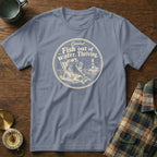 Slate blue t-shirt featuring a circular graphic of a fish lounging in a beach chair with text reading Fish out of water. Thriving.