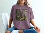 Bigfoot on a cliff overlooking a stormy sea, printed on a purple t-shirt.