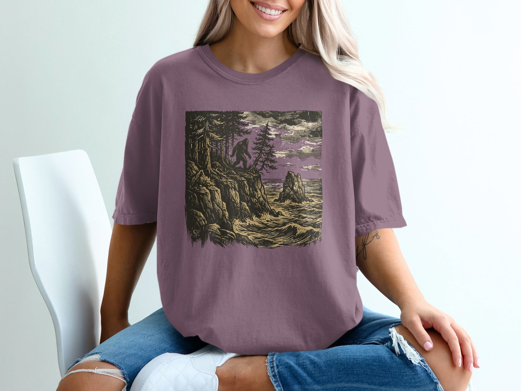 Bigfoot on a cliff overlooking a stormy sea, printed on a purple t-shirt.
