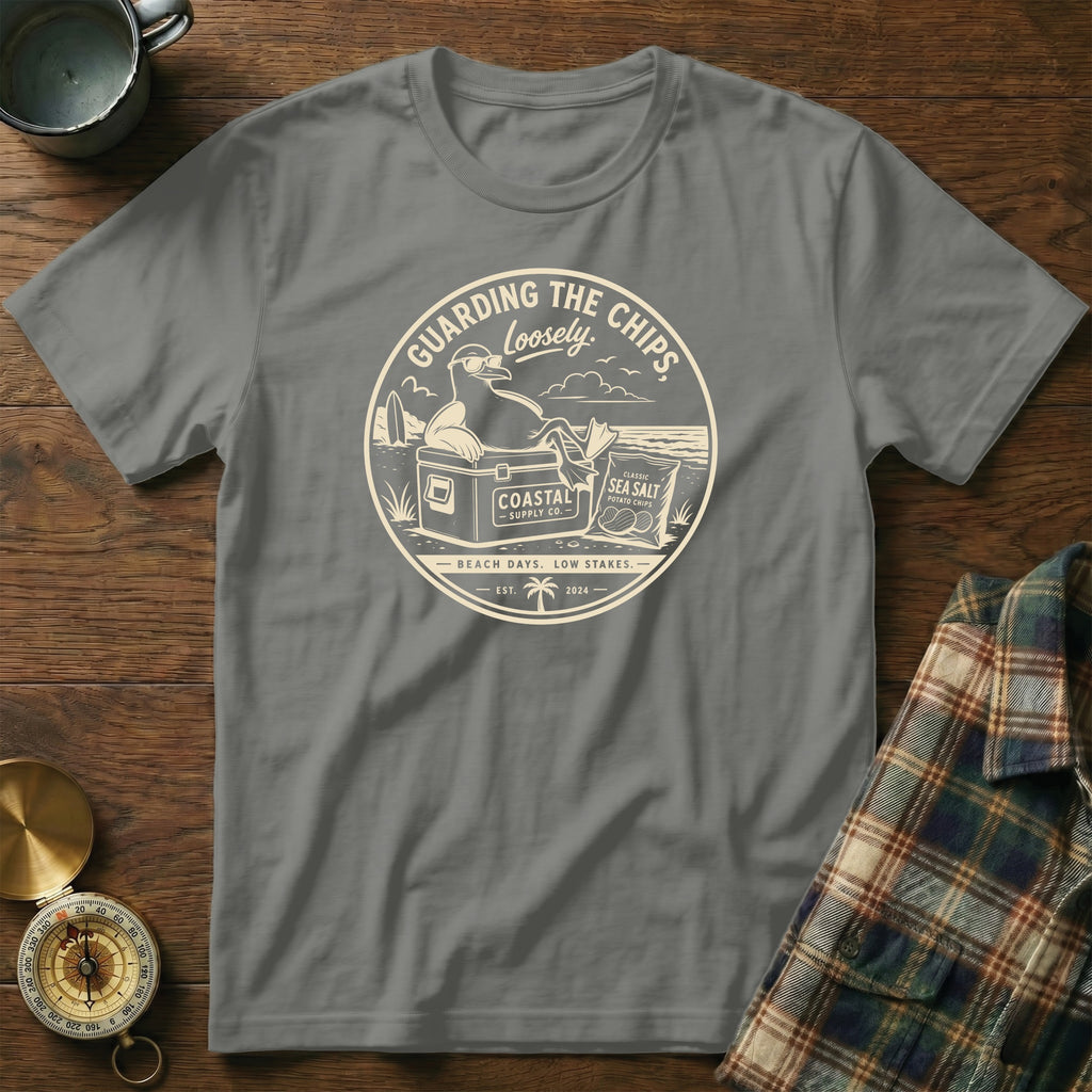 Gray t-shirt with a circular graphic of a seagull guarding chips on a beach.