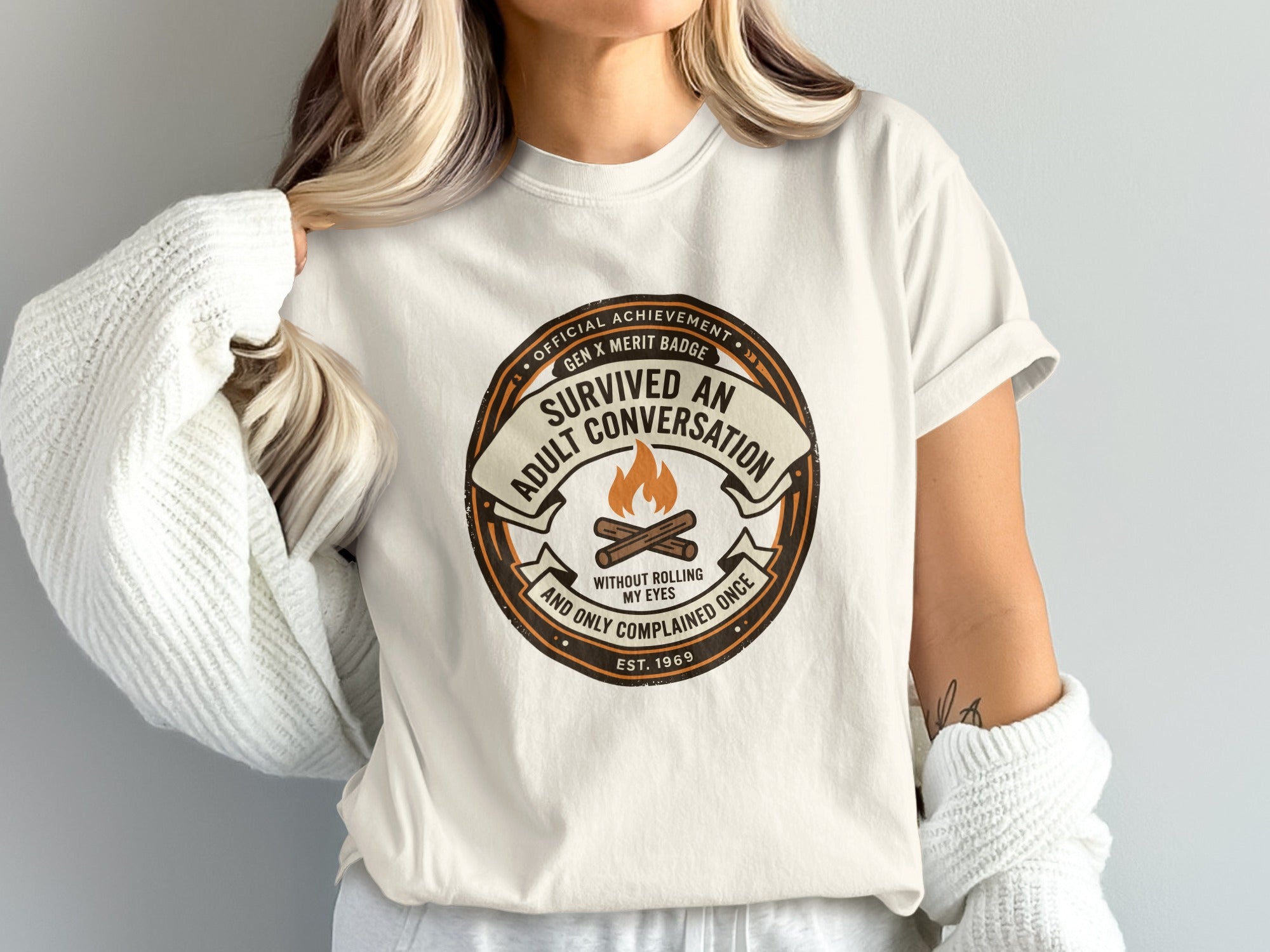 T-shirt with "Survived An Adult Conversation" merit badge design.