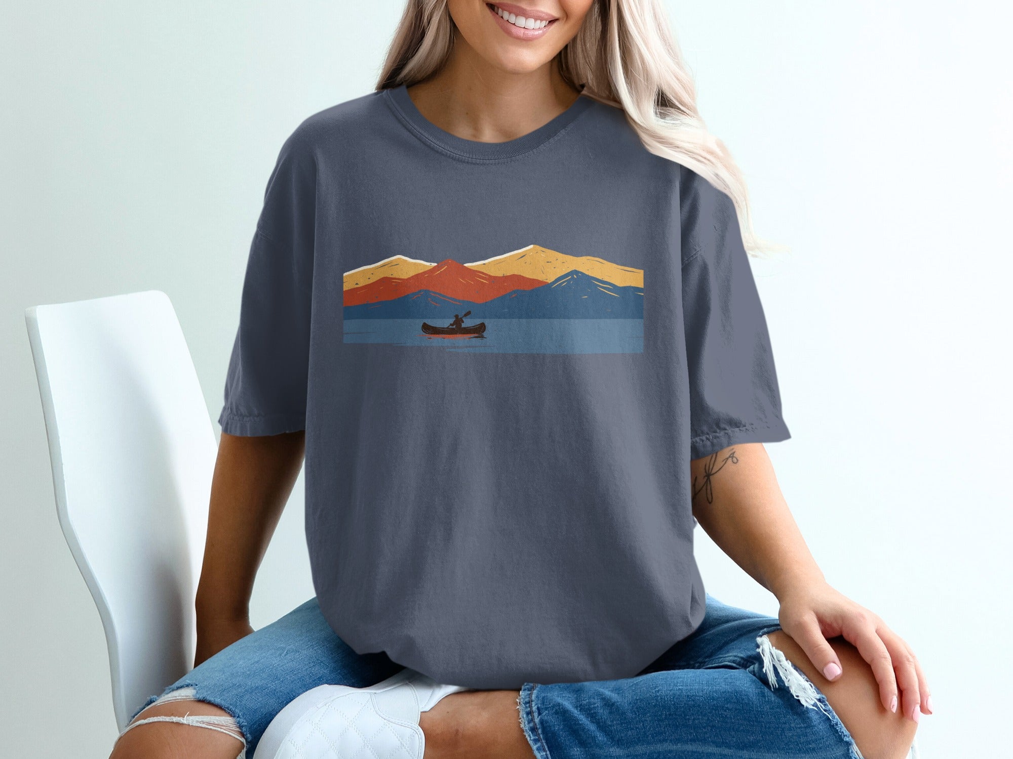 T-shirt with a vintage landscape graphic of a canoe on water and colorful mountains.