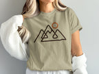 Tan t-shirt with abstract mountain line art and a circle representing a sun.