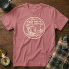Mauve short-sleeve t-shirt with a round graphic of a fish lounging in a beach chair and text reading Coastal Fish out of water. Thriving.