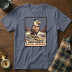 T-shirt graphic with eagle in striped shirt on surfboard, text "UNBOTHERED COASTAL AMERICANA".