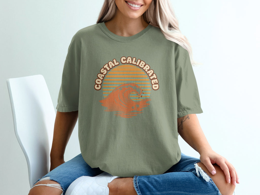 Green t-shirt with "Coastal Calibrated" text and wavy orange sunset graphic.