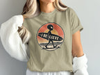Alien carrying a surfboard with text "I BELIEVE" on a vintage sunset background.