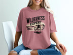 Pink t-shirt with "Wilderness Expert" text and beach scene graphic.