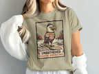 Eagle in hat and striped shirt surfs waves below text "UNBOTHERED COASTAL AMERICANA"