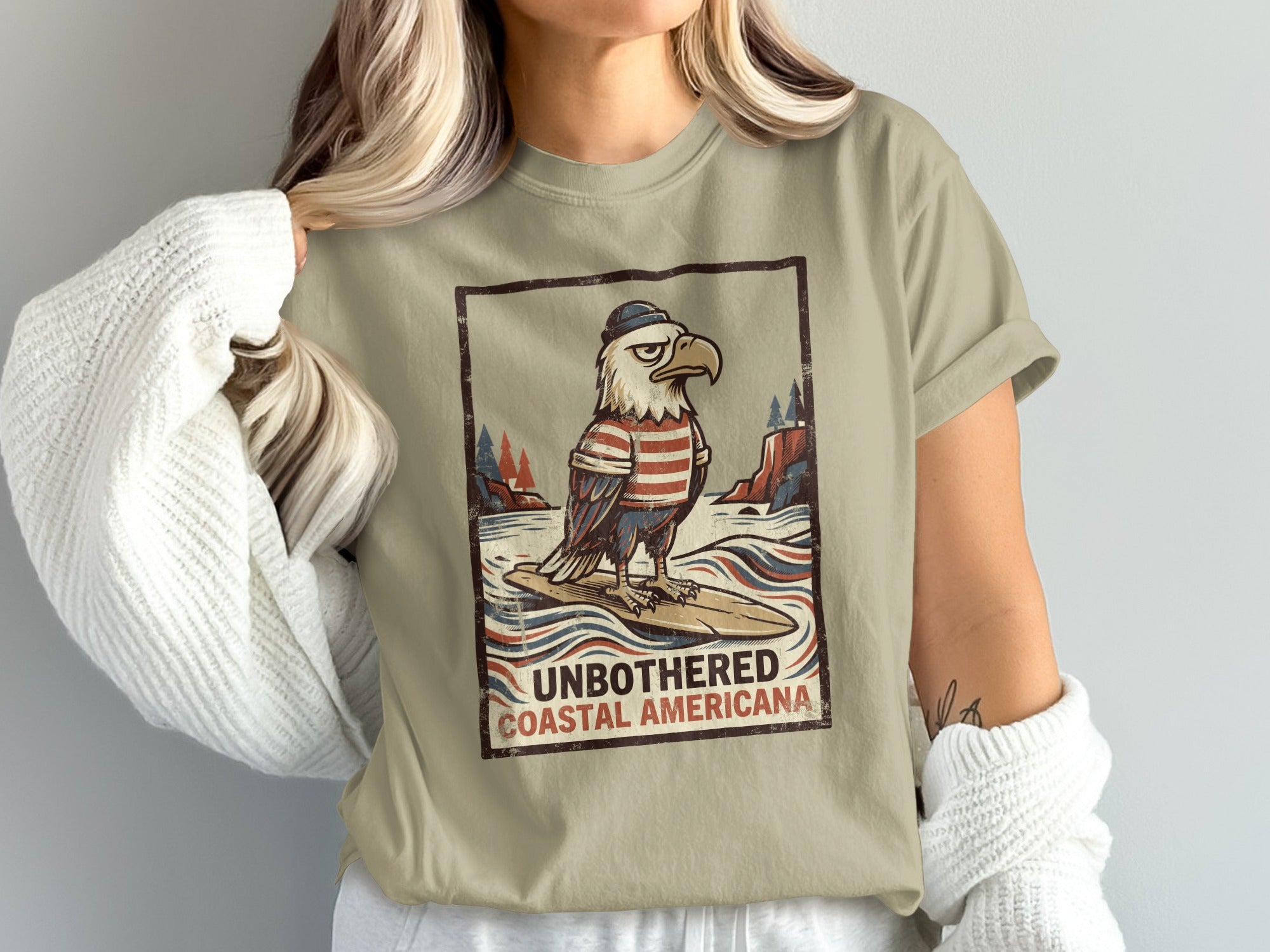 Eagle in hat and striped shirt surfs waves below text "UNBOTHERED COASTAL AMERICANA"