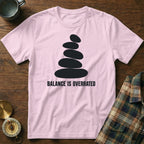 Pink t-shirt with black stacked stones graphic and "BALANCE IS OVERRATED" text.