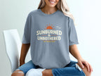 Light blue t-shirt with "Sunburned & Unbothered" text and sun graphic.